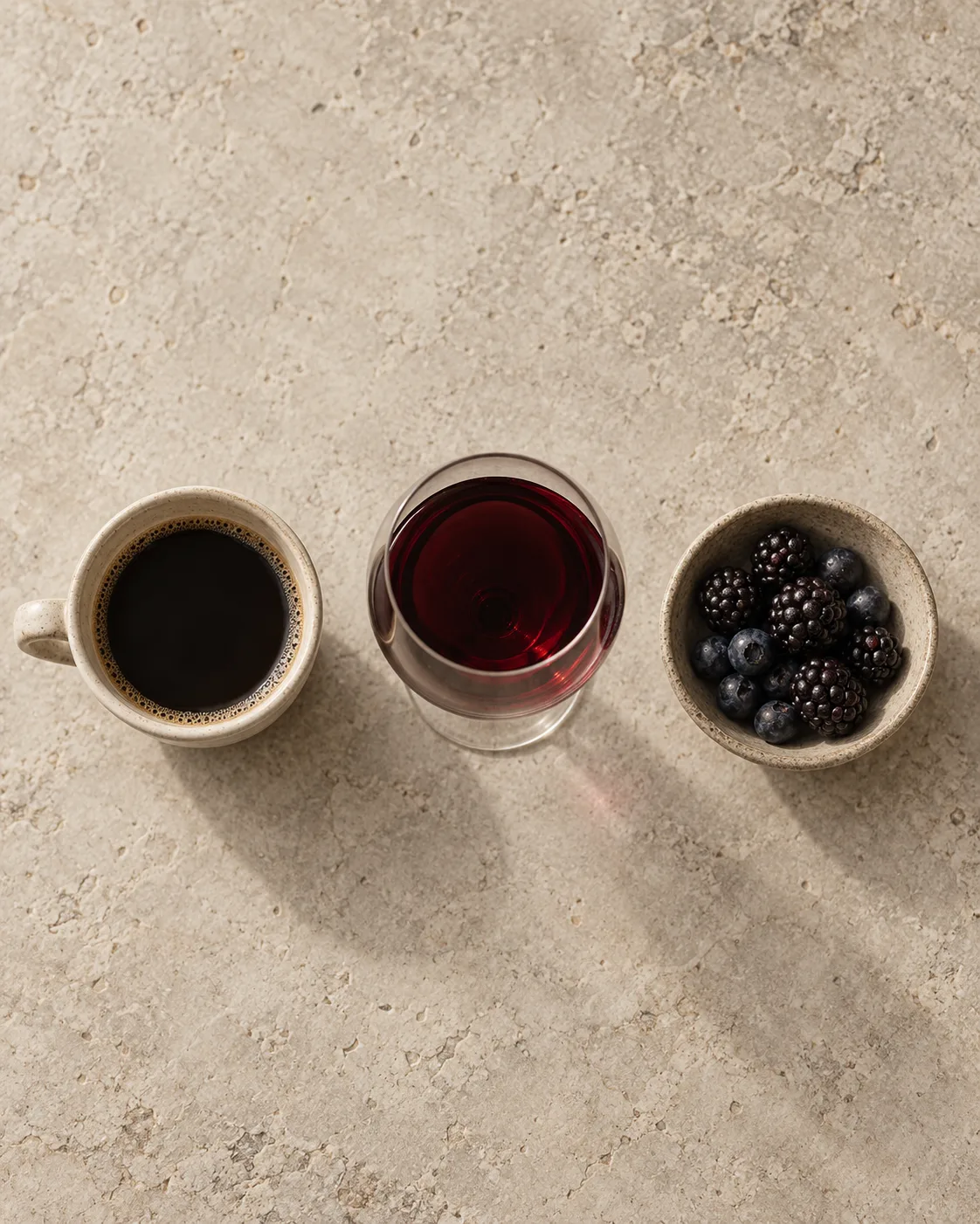 A cup of black coffee, a glass of red wine and a bowl of dark berries in a row